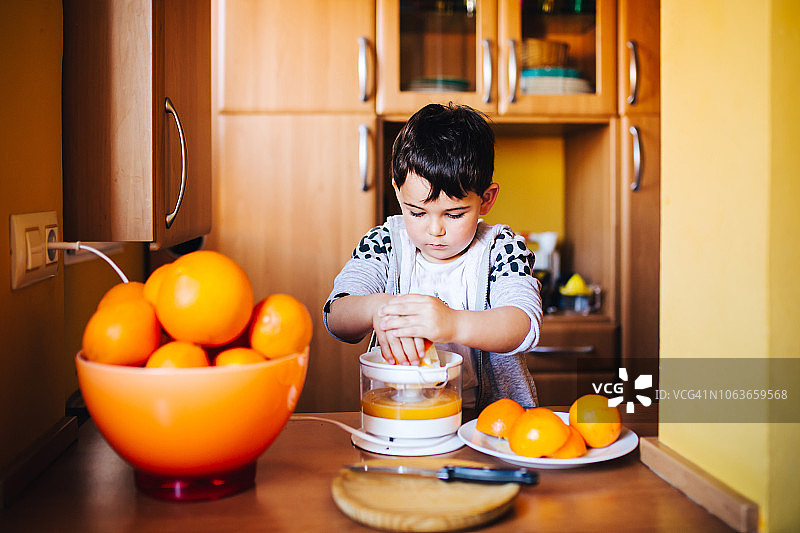 可爱的小男孩在厨房里准备橙汁图片素材