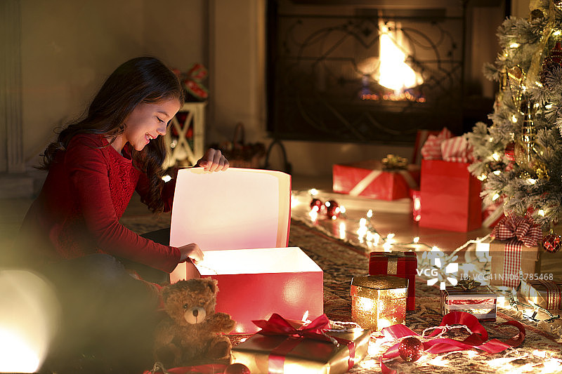 圣诞节期间，小女孩在圣诞树旁兴奋地打开礼物。图片素材