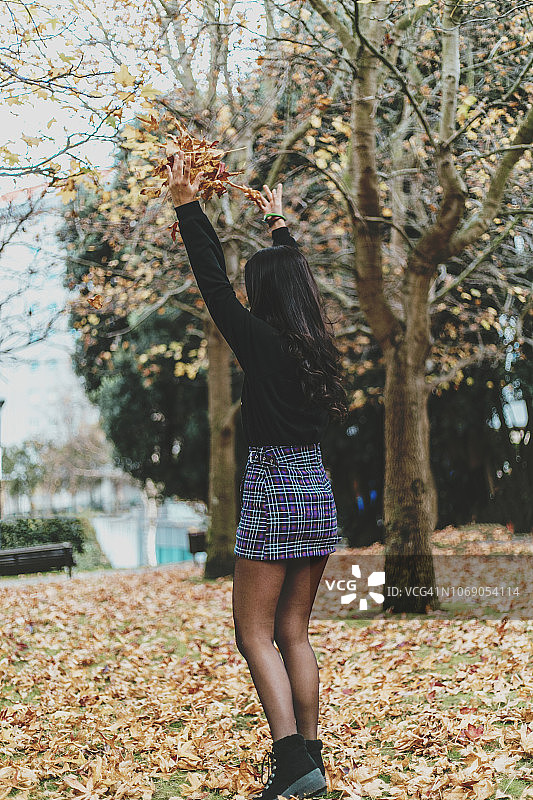 年轻的黑发女人在公园里玩秋叶图片素材