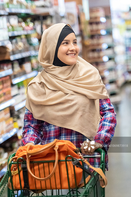 微笑的年轻穆斯林妇女在超市购物图片素材