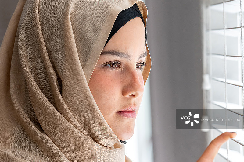 一名忧心忡忡的穆斯林年轻女子望着窗外图片素材
