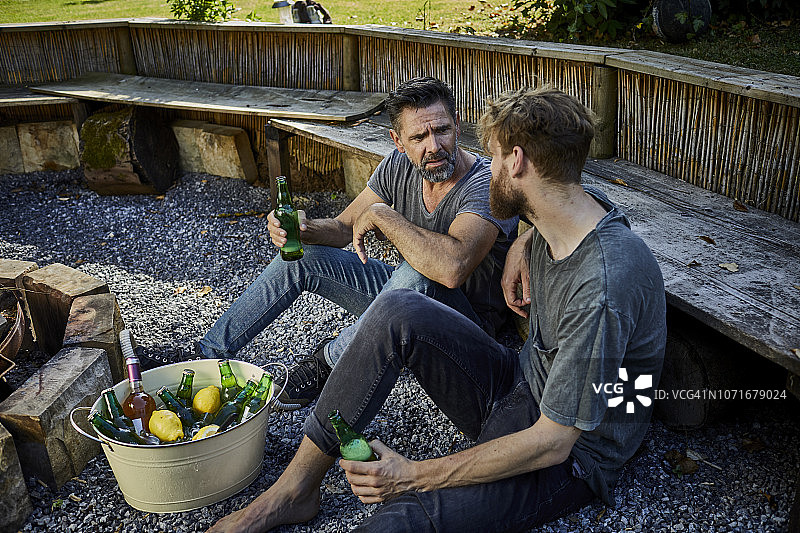 两个男人坐在花园里一边聊天一边喝啤酒图片素材