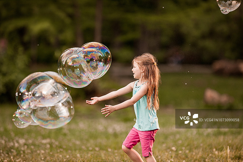 小女孩在公园里玩彩虹泡泡。图片素材