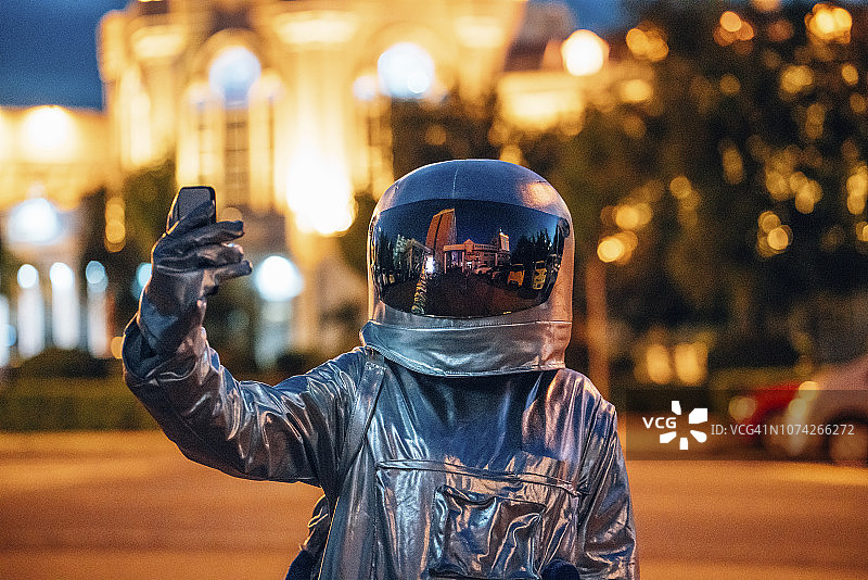 宇航员晚上在城市的街道上拿着智能手机图片素材