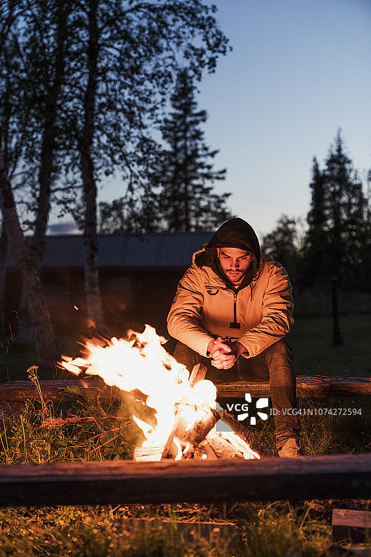 一个年轻人坐在篝火旁，看着火苗图片素材