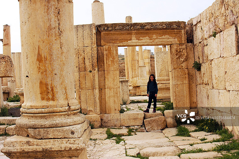 在约旦的安曼城堡，一个快乐的小女孩在一个漂亮的罗马风格的石门下面图片素材