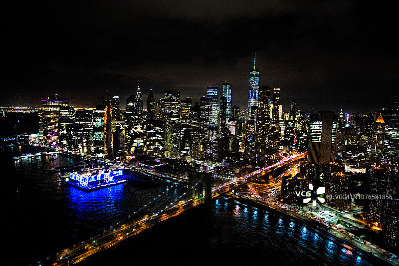 纽约布鲁克林大桥的鸟瞰图，从一架直升机在东河上方拍摄的夜晚图片素材