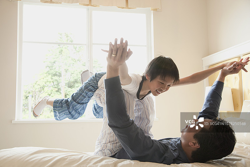 亚洲父亲和儿子在卧室的床上玩图片素材