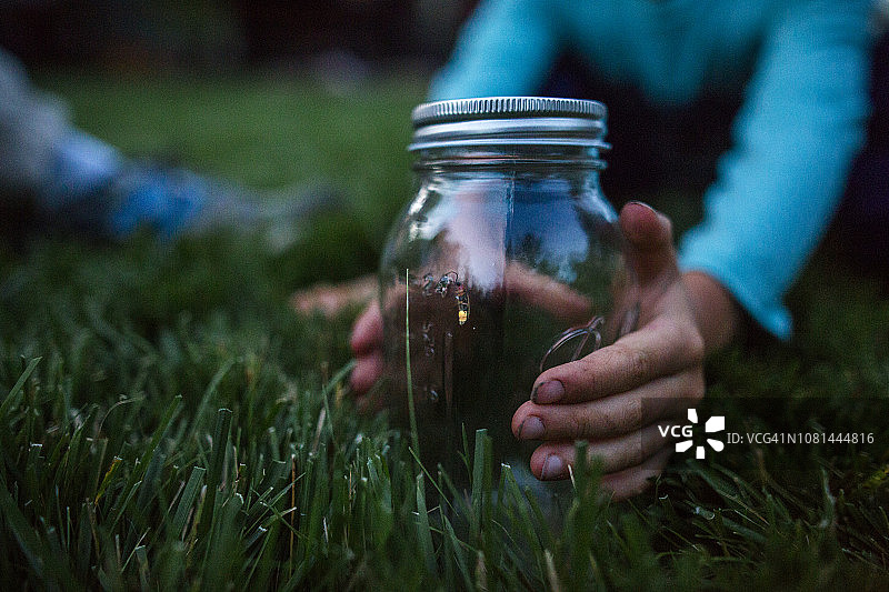 草地上，男孩双手抱着装有萤火虫的玻璃罐图片素材