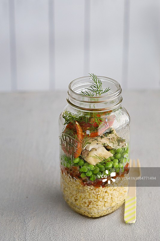 蒸粗麦粉沙拉配鱼，豌豆和西红柿，装在玻璃罐里图片素材