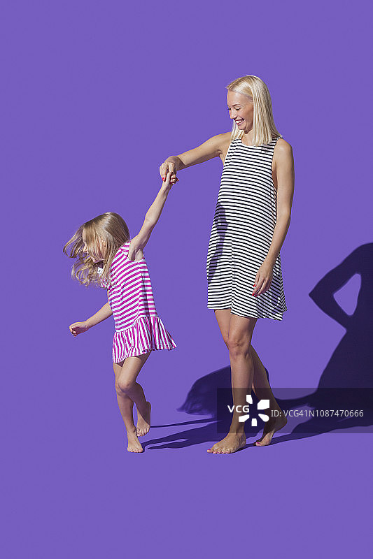 母亲和女儿穿着条纹裙子在紫色的背景上跳舞图片素材