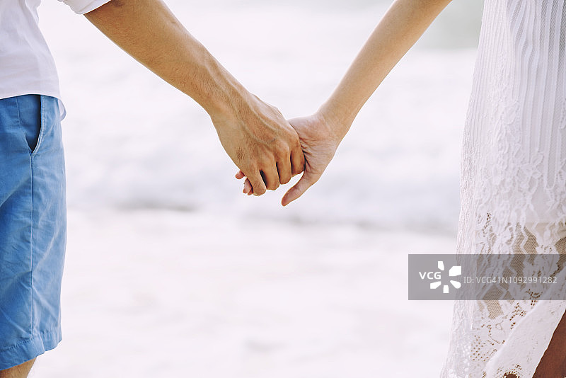 一对夫妇在日落时在海滩上牵手的特写。图片素材