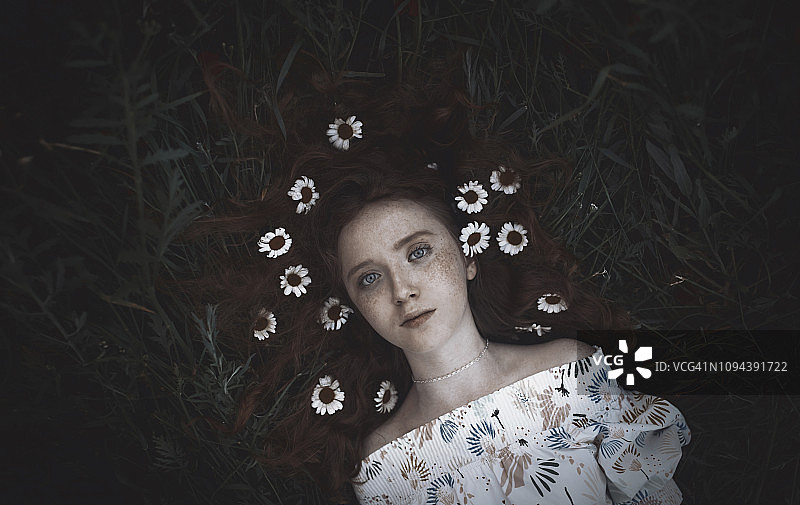 高角度肖像少女与洋甘菊躺在草地上图片素材
