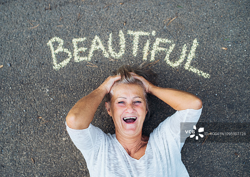 一个从上面俯视的高级女子躺在路上，用粉笔写着美丽的字在头顶。图片素材