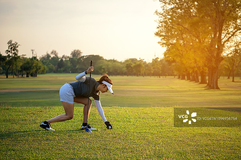 运动的亚洲高尔夫女选手在阳光明媚的日子里把高尔夫球与球杆放在高尔夫球场上为健康运动。生活方式和运动概念图片素材