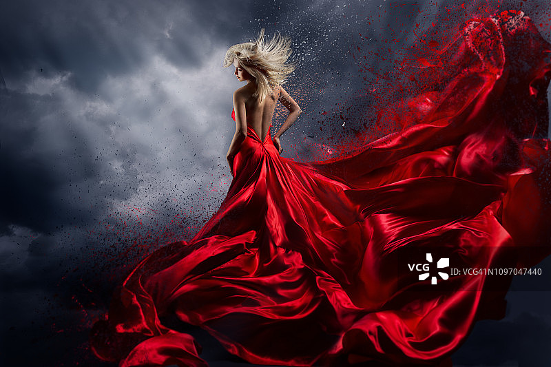 穿着红色连衣裙的女人在暴风雨的天空上跳舞，长裙飘动飞舞的织物图片素材