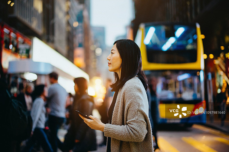 忙碌的年轻女商人用智能手机在城市中上下班，在香港市中心繁忙的城市街道上过马路图片素材