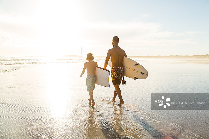 父亲和儿子一起在沙滩上冲浪图片素材