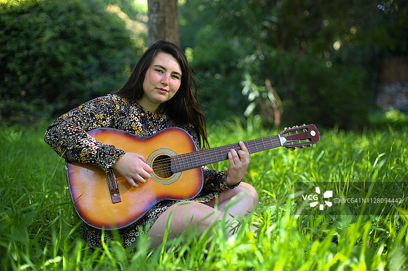 年轻女子坐在草地上弹吉他图片素材