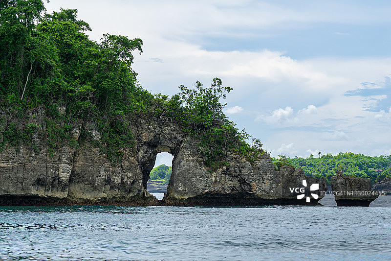 美丽的著名岩石与一个洞在水晶海滩与平静的海浪和水晶清澈的水在努沙佩尼达在巴厘岛，印度尼西亚。图片素材