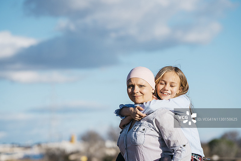 一位身患癌症的妇女站在她女儿旁边。一个女孩快乐地拥抱着一个女人图片素材