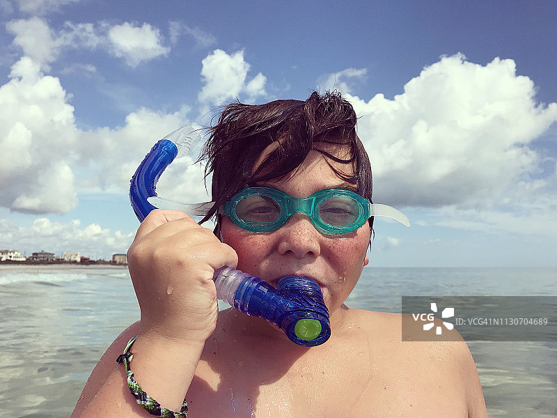 一个男孩在海滩上戴着护目镜和通气管的肖像图片素材