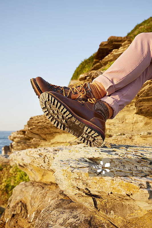 穿着登山靴的女人坐在海边的岩石上图片素材
