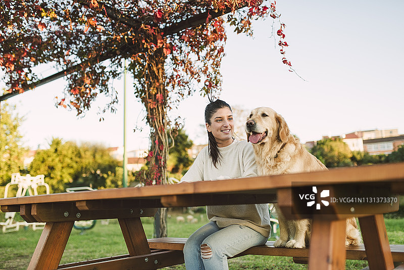 微笑的年轻女子和她的金毛猎犬在公园休息图片素材