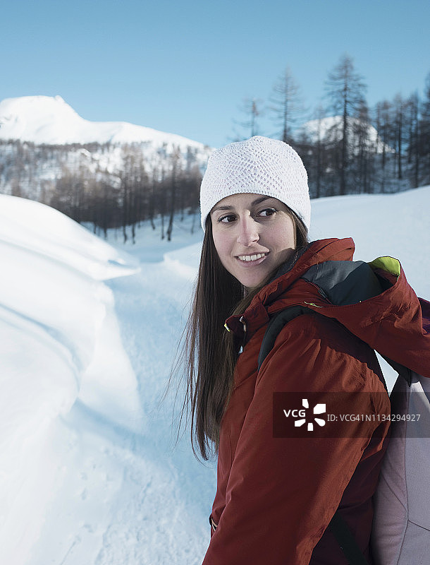 一名年轻女子戴着针织帽，在意大利皮埃蒙特的阿尔卑斯恰姆波里诺雪地里回望图片素材