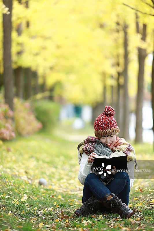 年轻女子在秋天的公园里看书图片素材