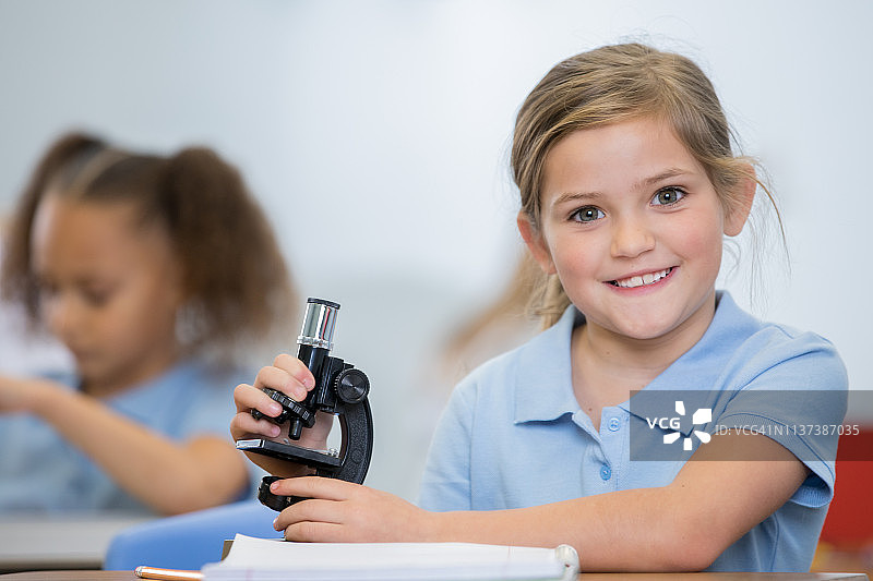 美丽的小学生小女孩微笑着在STEM课堂上使用显微镜图片素材