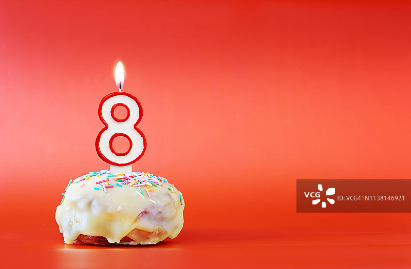 八年的生日。纸杯蛋糕，上面有燃烧着的白色蜡烛，形状是数字8。鲜艳的红色背景与复制空间图片素材