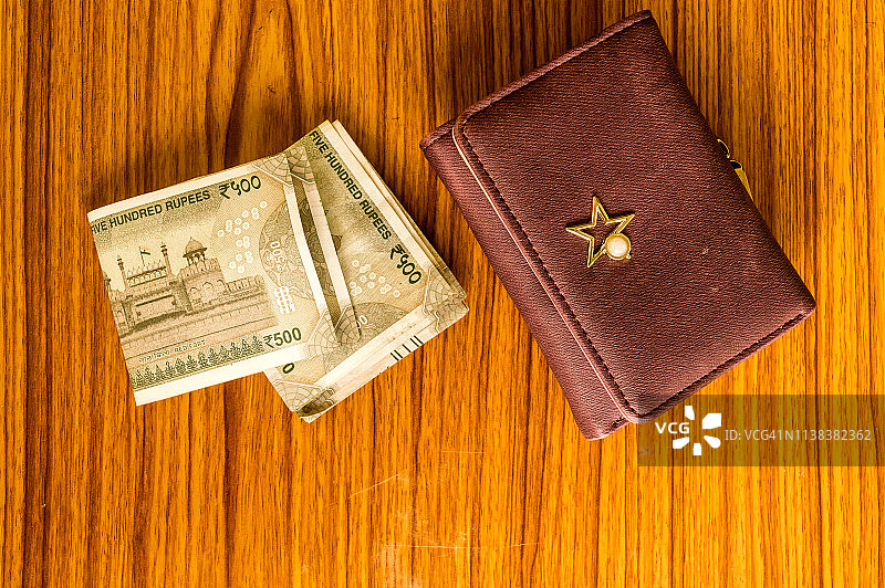木桌上的棕色皮包里装着印度500卢比现钞。企业财务经济概念。高角度视图与复制空间的文字在底部的图像图片素材