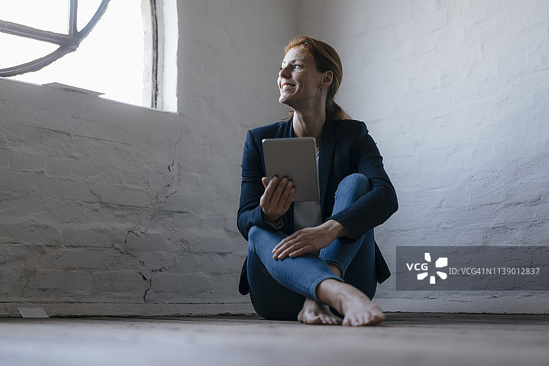 赤脚坐在办公室地板上使用平板电脑的女商人图片素材