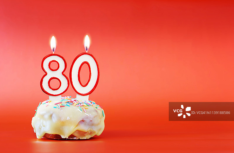 八十年的生日。用80号白色蜡烛做的纸杯蛋糕。鲜艳的红色背景与复制空间图片素材