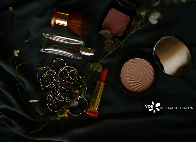 口红，粉饼，腮红，项链和香水瓶在深色丝绸背景图片素材