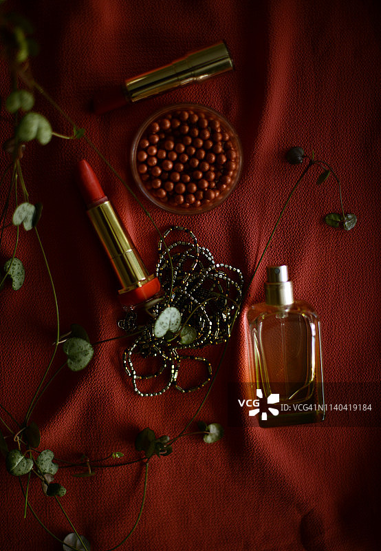 红色背景上的两支唇膏、古铜色粉末和一个香水瓶图片素材