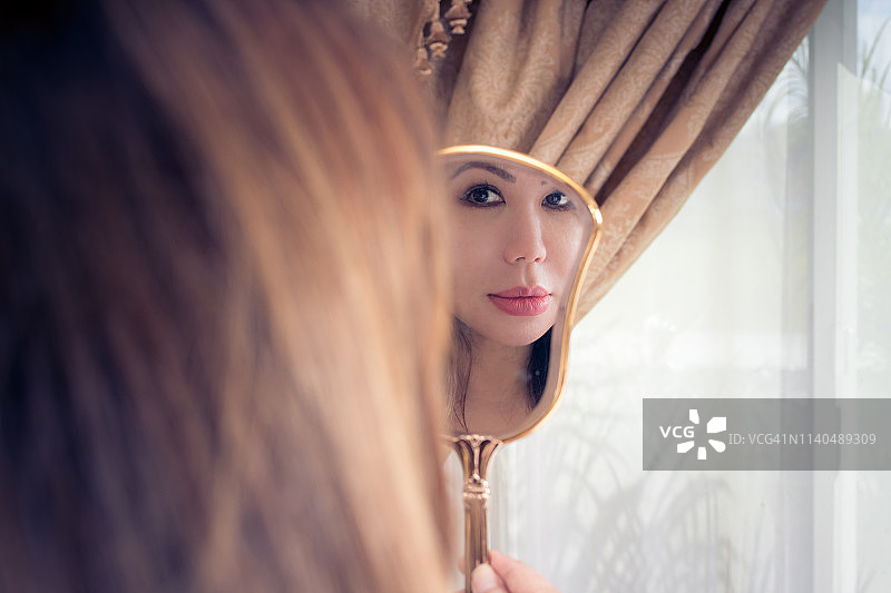 一个女人看着自己在一面古董手镜中的倒影图片素材