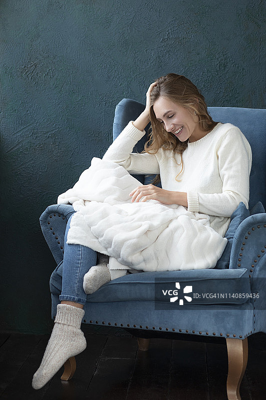 面带微笑的女人坐在扶手椅上，盖着白毯子图片素材