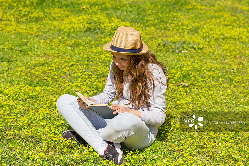 可爱的少女在绿色的草地上看书。有选择性的重点图片素材