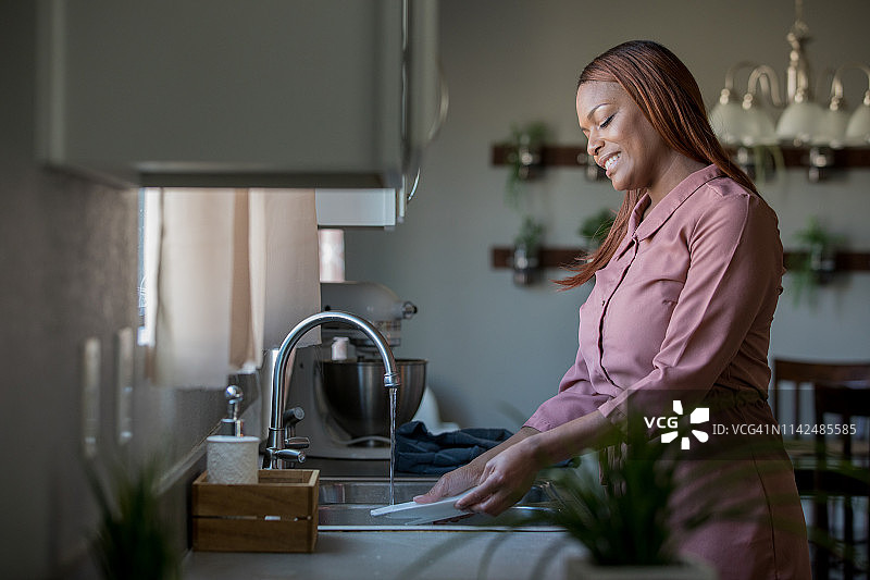 非洲裔美国成年妇女微笑着在厨房水槽洗盘子图片素材