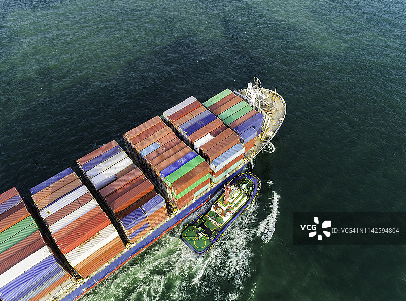 拖船在海港拖拽集装箱船，工作起重机桥装集装箱，用于物流，进出口，海运或运输。图片素材
