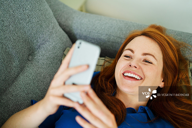 女人躺在沙发上用手机，微笑着图片素材