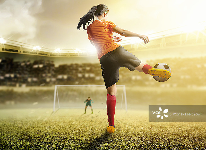 后视图亚洲足球运动员女子在橙色球衣踢球在禁区图片素材