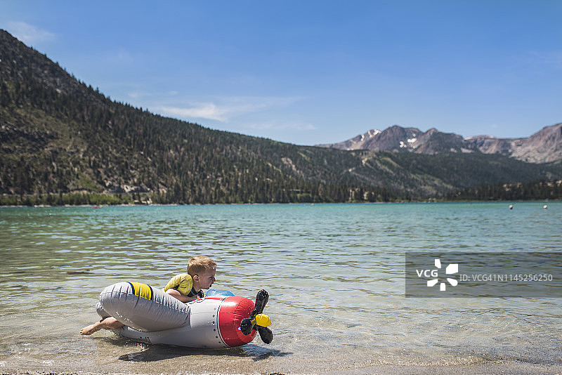 可爱的顽皮的男孩躺在充气飞机上，湖边的山在夏天图片素材