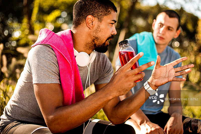 活跃的年轻运动员坐在公园里和他的朋友聊天，而从一个锻炼会议休息图片素材