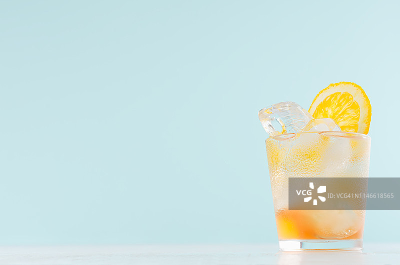 冷柳橙饮料在湿的小酒杯与橙子块，冰块在优雅柔和的浅绿色背景，复制空间。图片素材