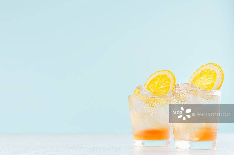新鲜的橙子鸡尾酒在雾蒙蒙的小酒杯与烈酒，切片的橙子，冰块在柔和的现代柔和的绿色背景。图片素材