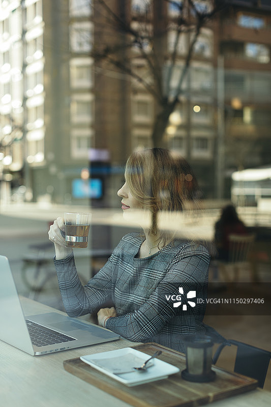 一个成熟的女商人在咖啡馆里拿着一杯茶和笔记本电脑图片素材