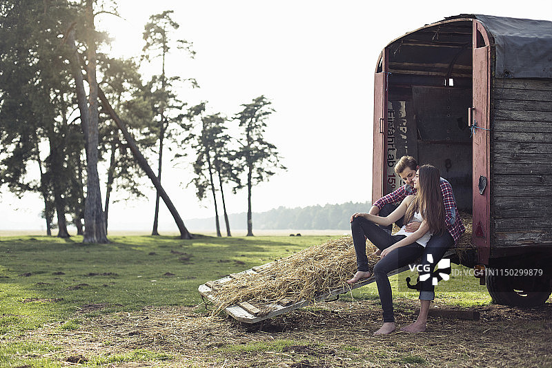 一对快乐的年轻夫妇坐在乡下的拖车上图片素材
